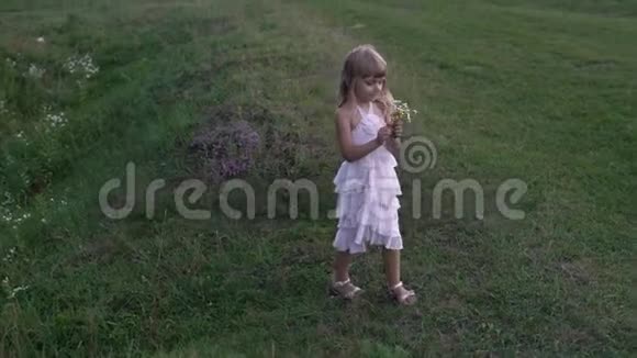 穿着白色裙子在绿茵场上玩花的小女孩视频的预览图