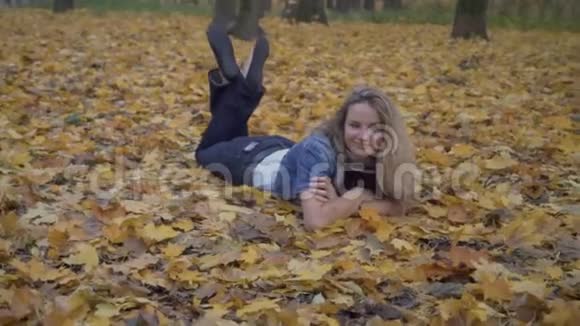 女人在秋天的森林里悠闲地躺在秋叶上视频的预览图