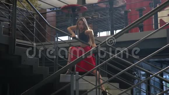 神秘的女孩在阳光下穿着红色的裙子黑色的顶部在商场的楼梯中间慢动作视频的预览图