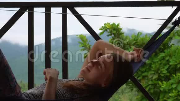 年轻女子在露台上的吊床上放松热带国家的假期视频的预览图