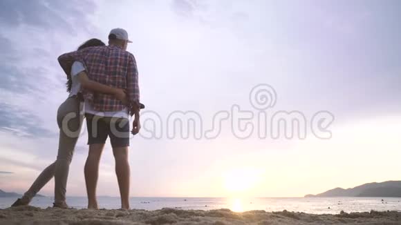 年轻的女人和男人在海滩上互相拥抱看着大海上的日落视频的预览图