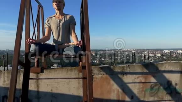 夏天金发男人在一座高工业建筑上训练瑜伽视频的预览图