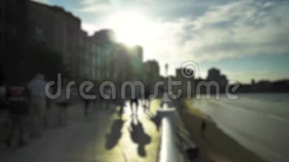 日落时带着步行的人蓝天上的戏剧性的云彩海浪和城市建筑使海滨变得明亮视频的预览图