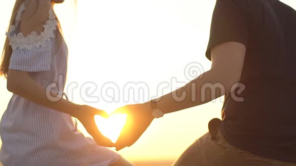 年轻夫妇在日落时展示心脏标志剪影慢动作视频的预览图