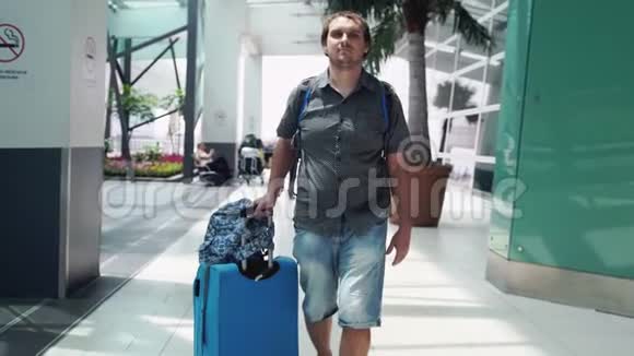 年轻快乐的帅哥背着背包在现代机场航站楼里拉着手提箱旅行的帅哥走了视频的预览图