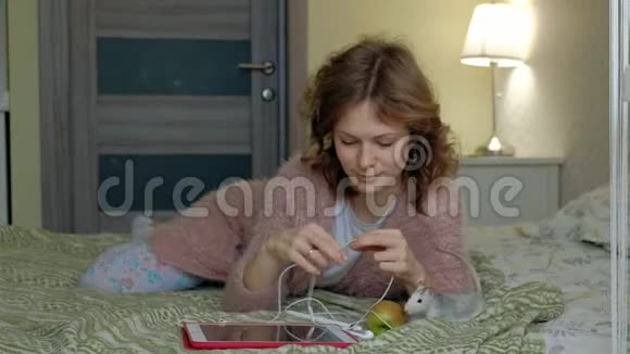 快乐女孩在卧室里用耳机和平板电脑在家工作在床上玩宠物老鼠网上冲浪视频的预览图
