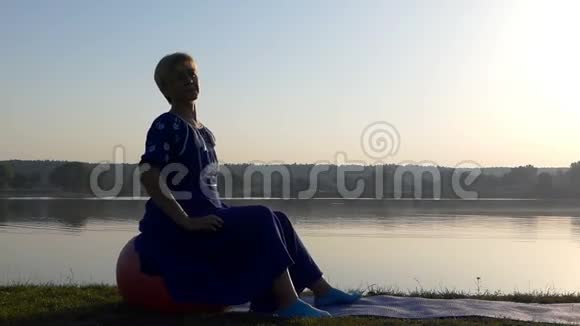 一个美丽的女人坐在湖边的一个红色的球上视频的预览图