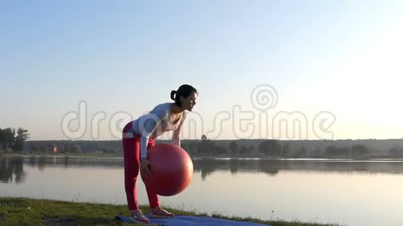 一个运动的女人在日落时弯着腰手里拿着红色的健身球视频的预览图