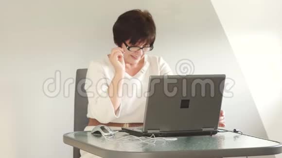 在办公室工作的女商人仔细看着眼镜上方的笔记本电脑屏幕微笑商务小姐视频的预览图