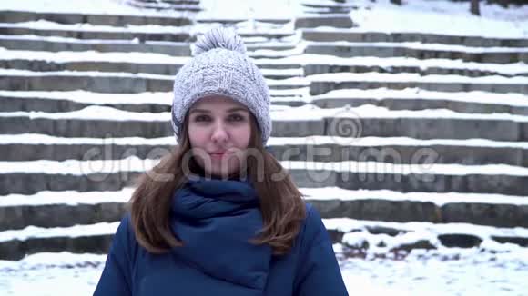 戴着冬帽的漂亮女人微笑着站在森林里的雪地上背景是雪楼梯一幅肖像画视频的预览图