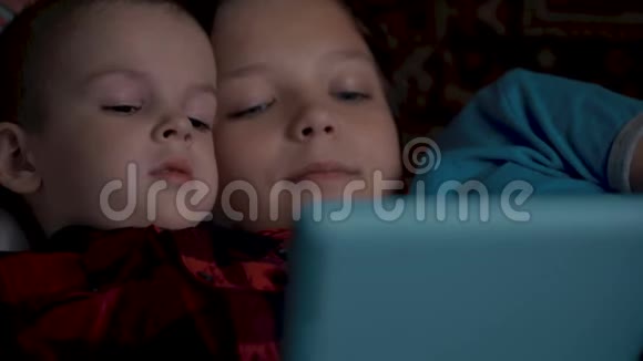 两个男孩使用平板电脑躺在沙发上视频的预览图