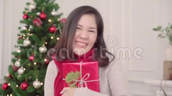圣诞佳节快乐的年轻亚洲女人在家的客厅里捧着圣诞礼物微笑着拍照视频的预览图