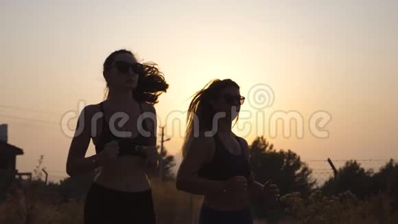 日落时分两个年轻女孩在户外跑步年轻的运动女性在乡间路慢跑女运动员训练视频的预览图