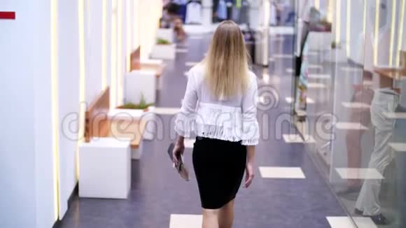 女孩高个子漂亮的金发女人沿着商店的窗户沿着购物中心的大厅走着视频的预览图