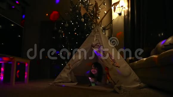 一个小女孩躺在地上躺在一个圣诞树的背景下坐在帐篷里讲视频视频的预览图