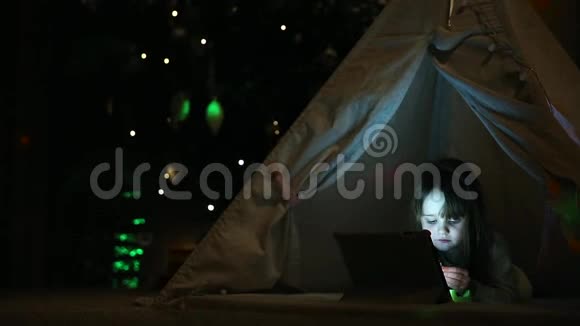 一个小女孩躺在地上躺在一个圣诞树的背景下坐在帐篷里讲视频视频的预览图