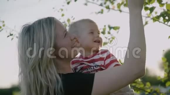 可爱的母亲抱着小儿子在怀里玩桦的叶子俄罗斯桦树作为背景慢动作4k视频的预览图
