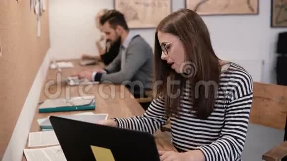 年轻漂亮的女孩正在使用笔记本电脑处理文件在现代的创业办公室做笔记视频的预览图