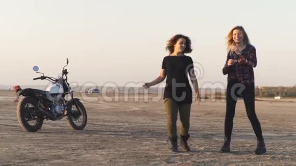 两个年轻漂亮的女人在日落或日出时在沙漠中跳舞摩托车背景视频的预览图
