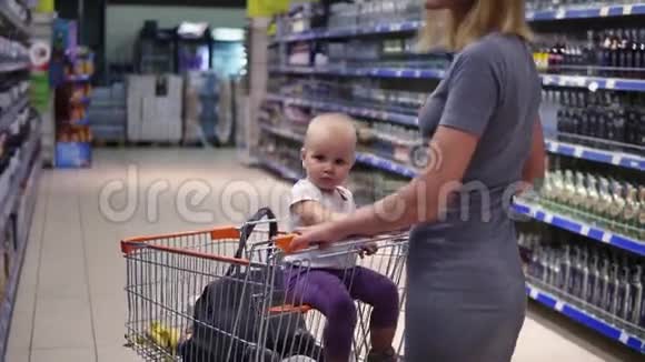 饮料部的年轻妈妈正在挑选一瓶葡萄酒而她的小宝宝正坐在购物车里视频的预览图