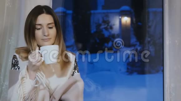 冬天的夜晚美丽的女孩在窗台上喝杯咖啡放松视频的预览图