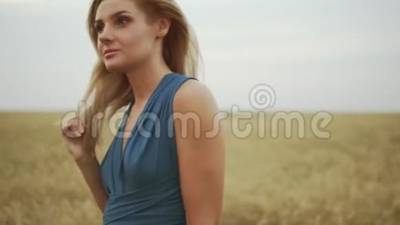 从金色麦田里走过的一件蓝色裙子中看到一位迷人的金发年轻女子的特写镜头自由概念视频的预览图