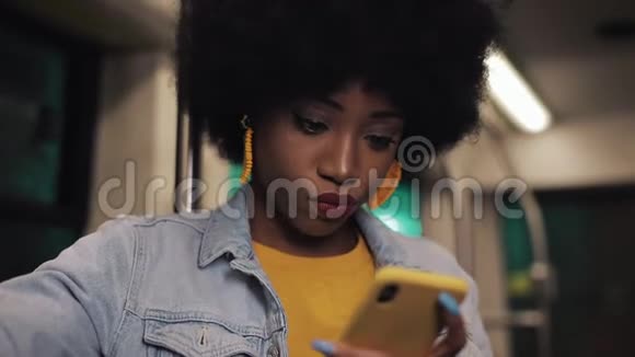 漂亮的非裔美国年轻女性握着扶手在公共交通中使用智能手机晚上视频的预览图