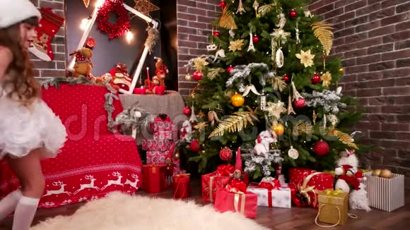 小女孩在圣诞树下发现礼物女儿穿着精灵圣诞老人的服装为新年选择惊喜视频的预览图