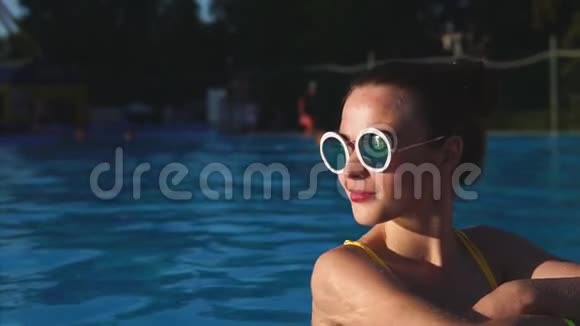在游泳池里穿着黄色泳衣和太阳镜的时尚迷人的女人视频的预览图