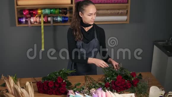 年轻的女性花店用漂亮的红玫瑰布置现代花束慢镜头视频的预览图