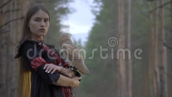 一个穿着衣服的女孩和一只甜美的浅棕色猫头鹰镜头站在森林的中央视频的预览图