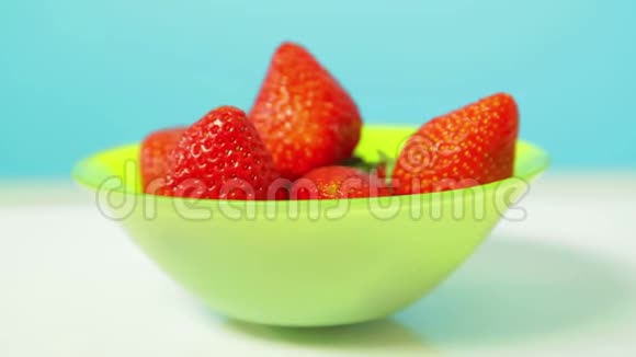 绿色盘子里的成熟多汁草莓在蓝色背景下旋转成一个圆圈视频的预览图