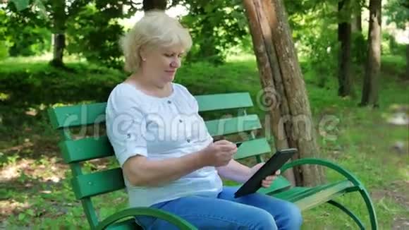 老妇人在公园里坐在长凳上网上买东西高级女性购物通过互联网使用平板电脑视频的预览图