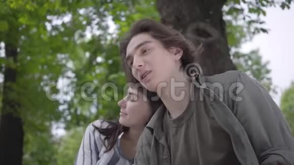 年轻快乐的一对穿着便服的夫妇在公园里聚在一起约会坐在长椅上的情侣视频的预览图
