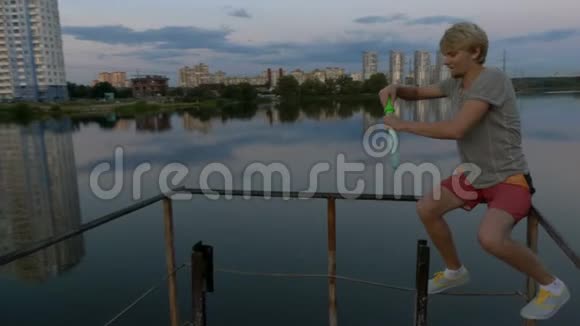 年轻人坐在湖边的篱笆上做肥皂泡视频的预览图