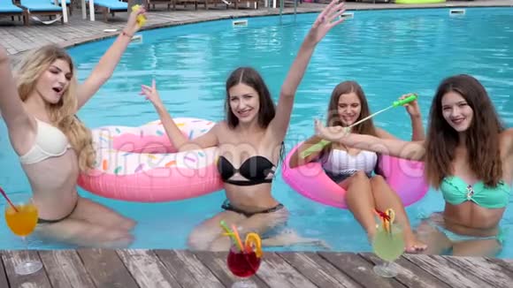 在度假村举行鸡尾酒会女朋友穿着泳衣在泳池边玩得很开心笑的女孩坐在充气戒指上视频的预览图