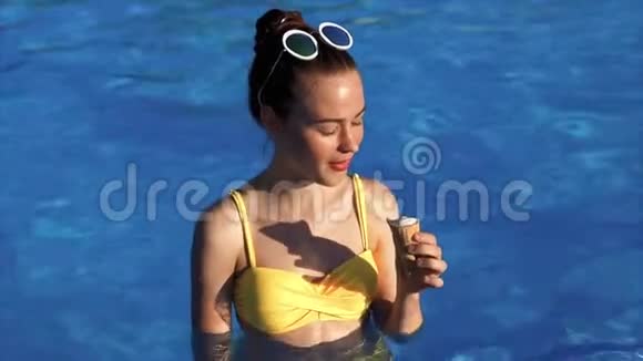 年轻女子在游泳池里按喇叭吃开胃的奶油冰淇淋视频的预览图