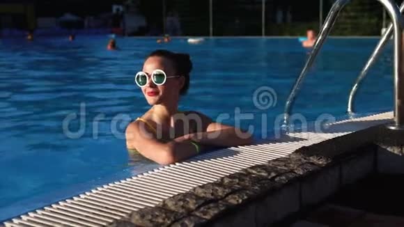 一位戴着时髦眼镜的美女在游泳池里她享受着温暖的一天视频的预览图