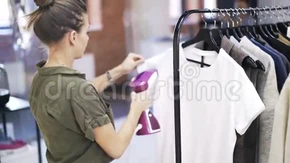 一个年轻的女人在商店里蒸着一件白色的恤视频的预览图