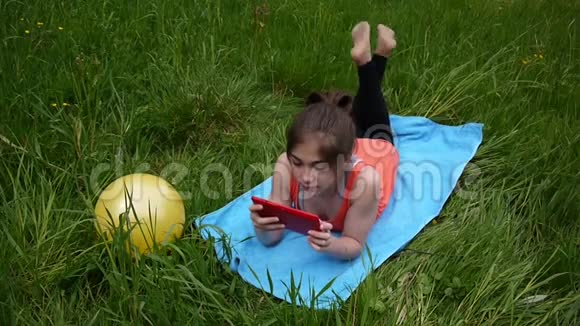 轻松的年轻女孩使用数字平板电脑在乡村领域可爱的少年躺在草地上录像片高清拍摄视频的预览图