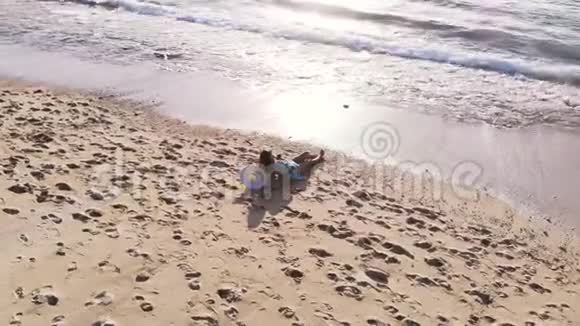 无人驾驶飞机观看年轻的黑发女子太阳镜躺在热带天堂海滩和使用手机期间视频的预览图