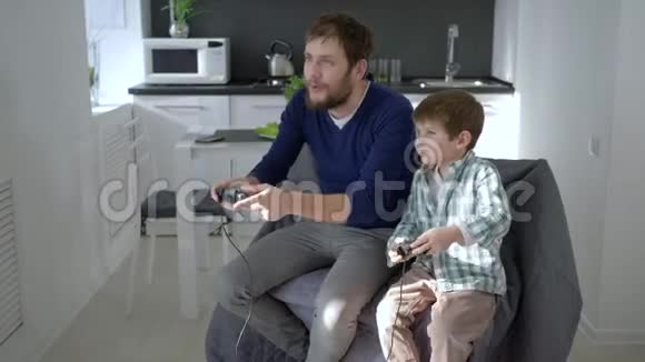 父亲带着孩子带着游戏控制器抱在怀里在家玩电子游戏视频的预览图