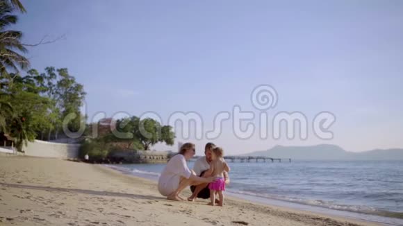 幸福的一家人在海滩上牵着手挥舞着一个小女孩妈妈爸爸女儿在海滩上散步概念视频的预览图