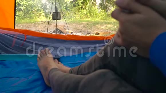 帐篷里的女人喝热茶水壶在她面前的炉火上加热视频的预览图