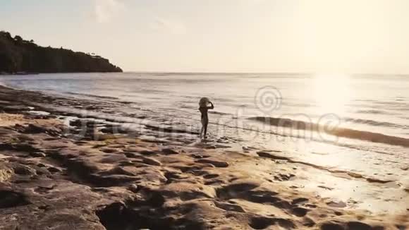 无人驾驶飞机俯瞰年轻有思想的女人戴着帽子站在海滩上观看海景视频的预览图