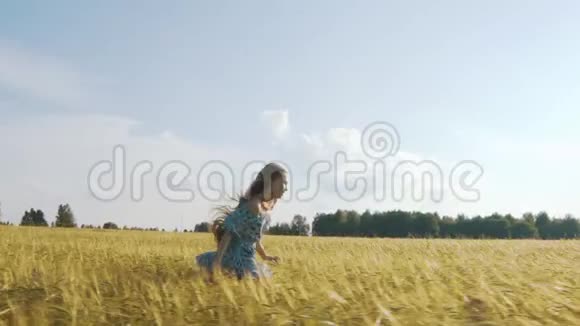 一个年轻的女孩开心地笑着在日落时沿着金色的麦田奔跑慢动作视频的预览图