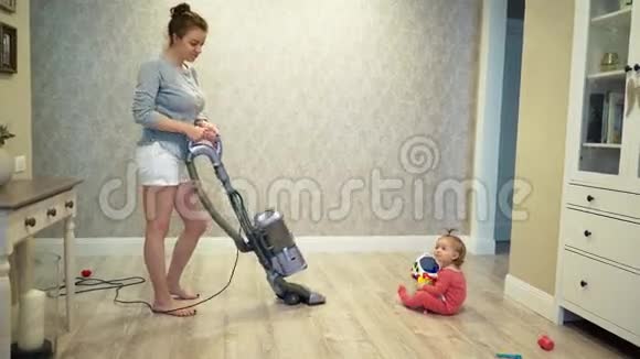 妈妈用吸尘器清理地板上的灰尘一个小孩子她的女儿正在附近玩耍视频的预览图