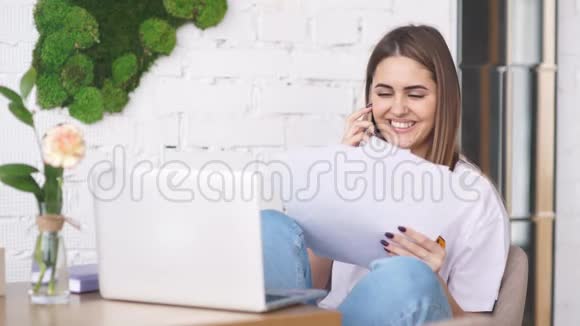 年轻的自由职业者女孩打电话拿着文件笔记本电脑在桌子上视频的预览图