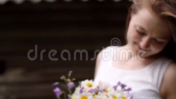 一个手里拿着野花的女孩站在木屋的背景上视频的预览图