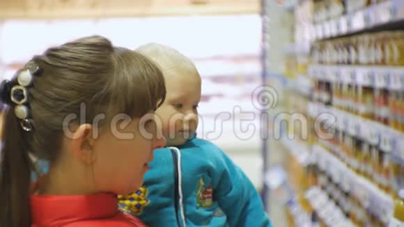 可爱的白种人妇女选择婴儿食品在超市抱着婴儿怀里妈妈带孩子的特写镜头视频的预览图